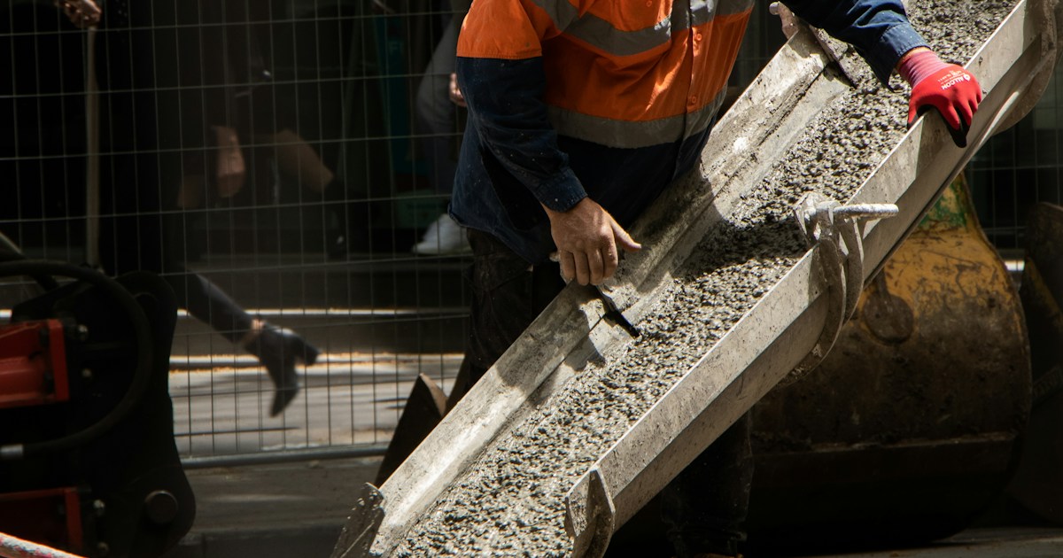 Trabajador de construcción con chaleco naranja guiando concreto húmedo por canal de camión mezclador