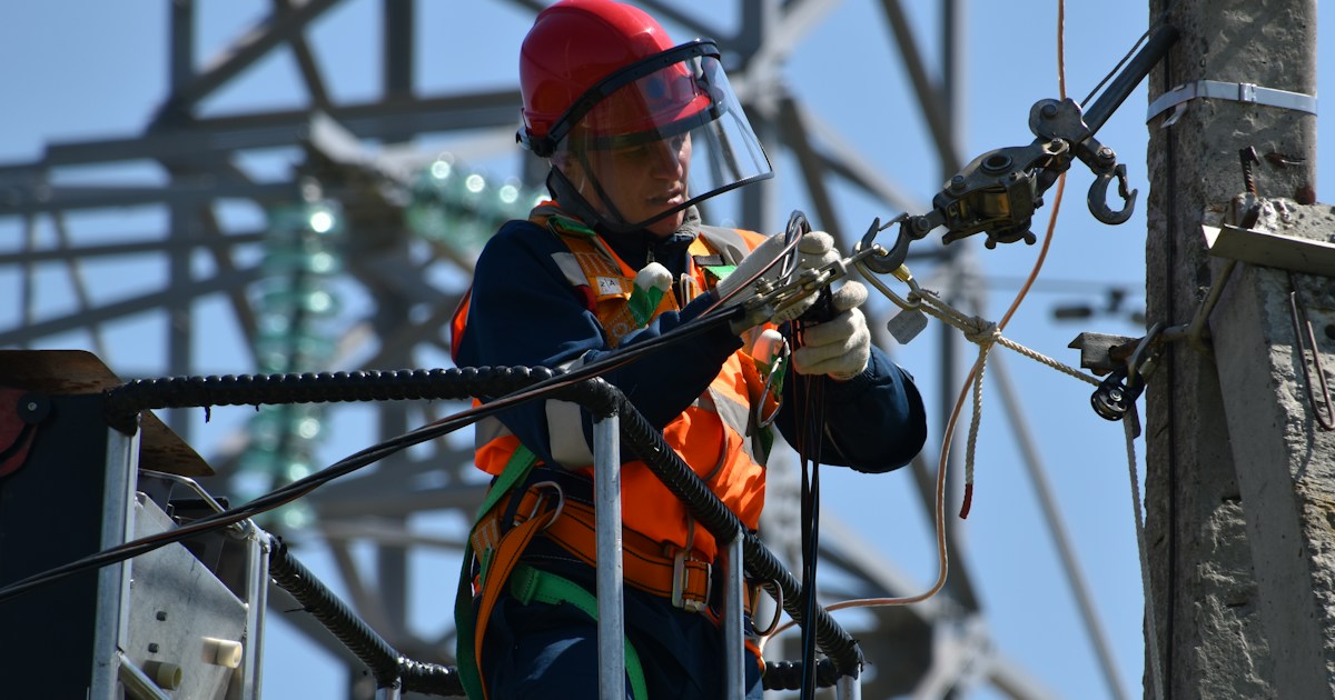 Liniero eléctrico con equipo de seguridad trabajando en líneas de alta tensión