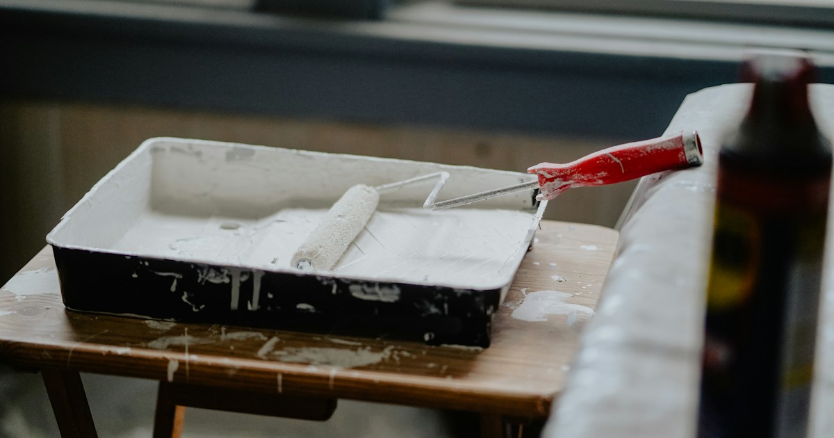 Paint roller and tray with white paint on workbench at job site