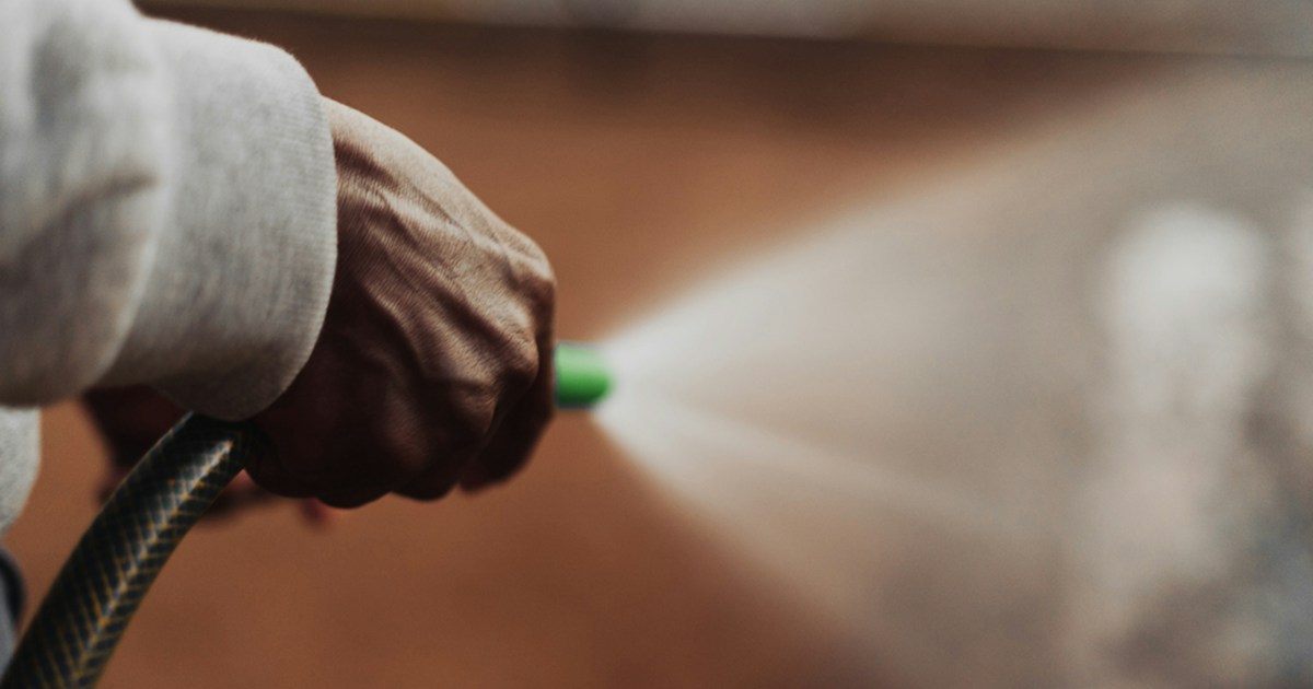 Close-up of a hand holding a pressure washer nozzle spraying high-pressure water