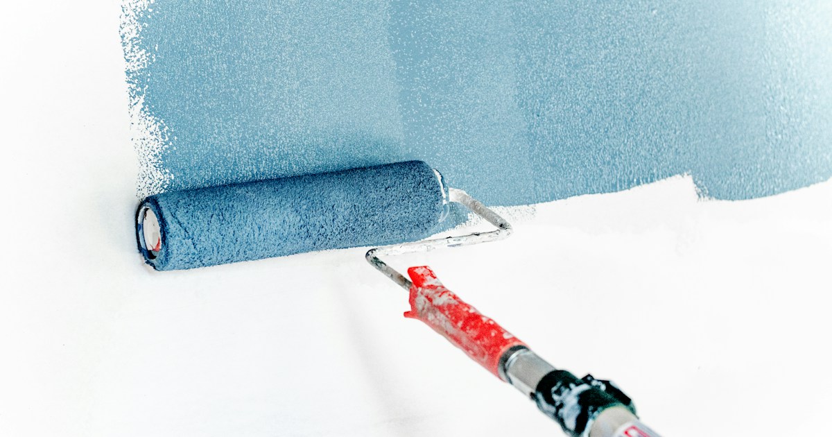 Rodillo de pintura azul aplicando pintura en superficie de pared blanca
