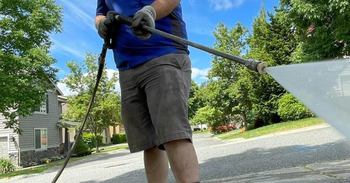 Hombre lavando un driveway residencial con una pistola de alta presión en día soleado