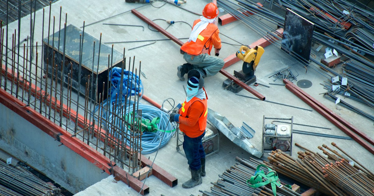 Trabajadores de construcción con chalecos de seguridad naranja trabajando con varilla y concreto en obra comercial