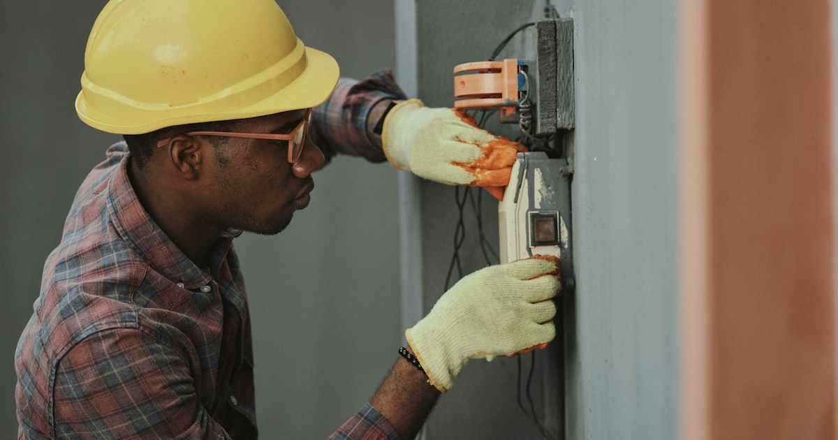 Electrician with hard hat and safety glasses installing electrical panel