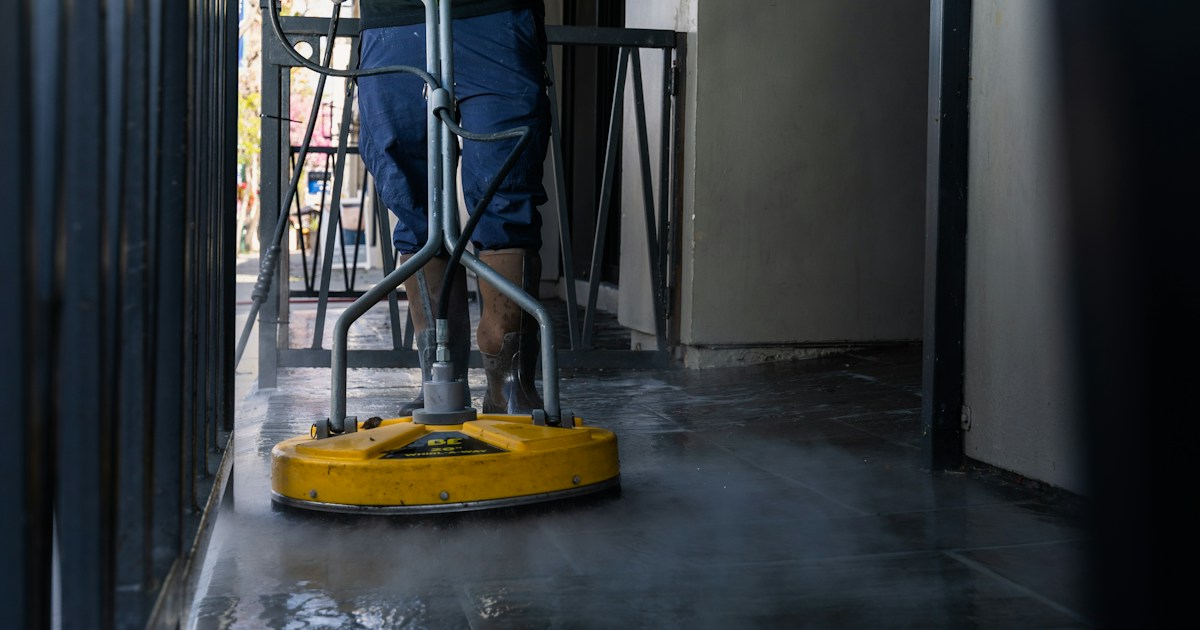 Trabajador profesional de lavado a presión usando un limpiador de superficie amarillo en piso comercial